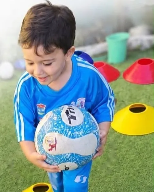 Menino com uniforme de futebol segurando a bola no gramado